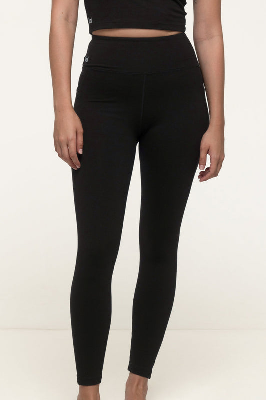 Closeup of a woman in a black sustainable activewear set wearing thick black soft leggings with pockets. #color_black