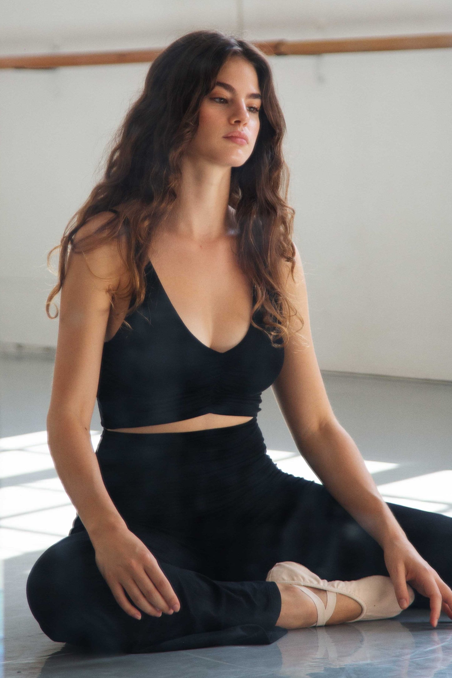 Ballerina in a black outfit sitting on the floor in a dance studio.