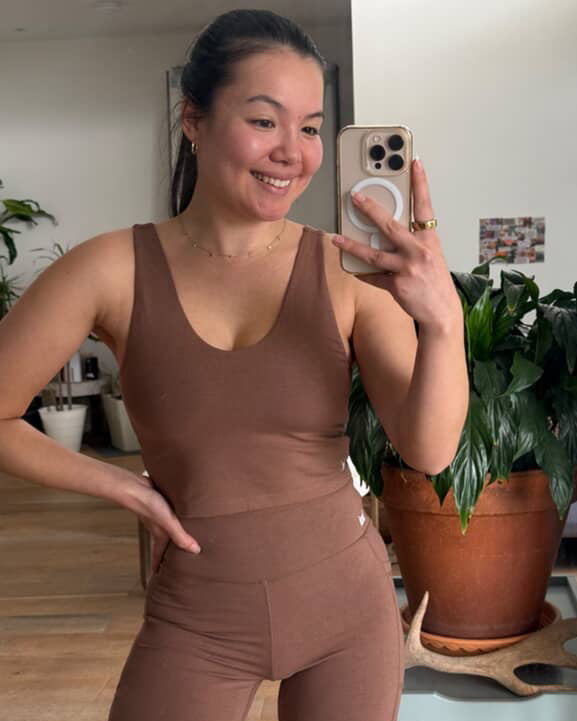 Customer taking a mirror selfie wearing a brown tank top and shorts set in natural bamboo activewear. 