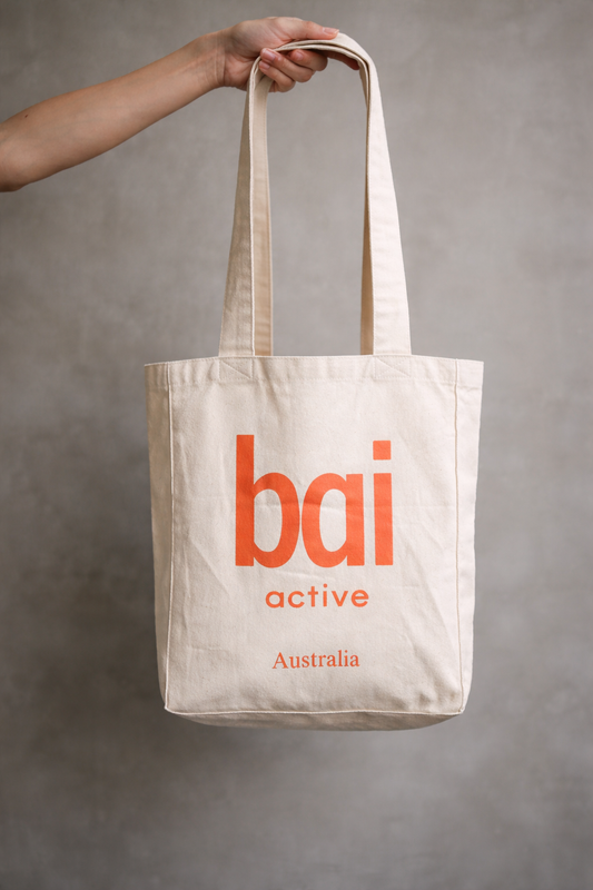 Beige tote bag with 'bai active Australia' text held by a hand against a gray background