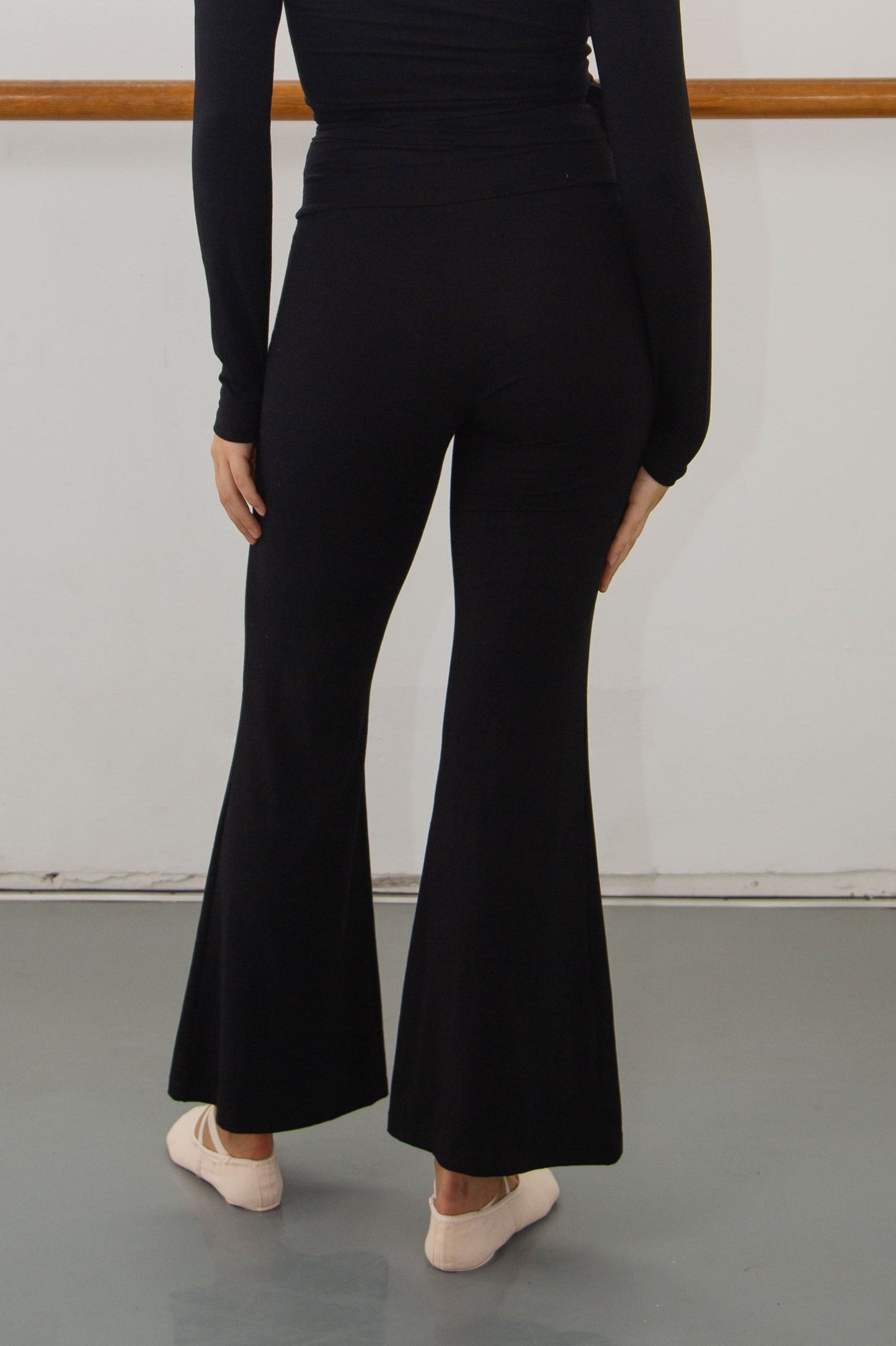 Woman wearing a black modal fabric outfit standing in a dance studio and a barre.