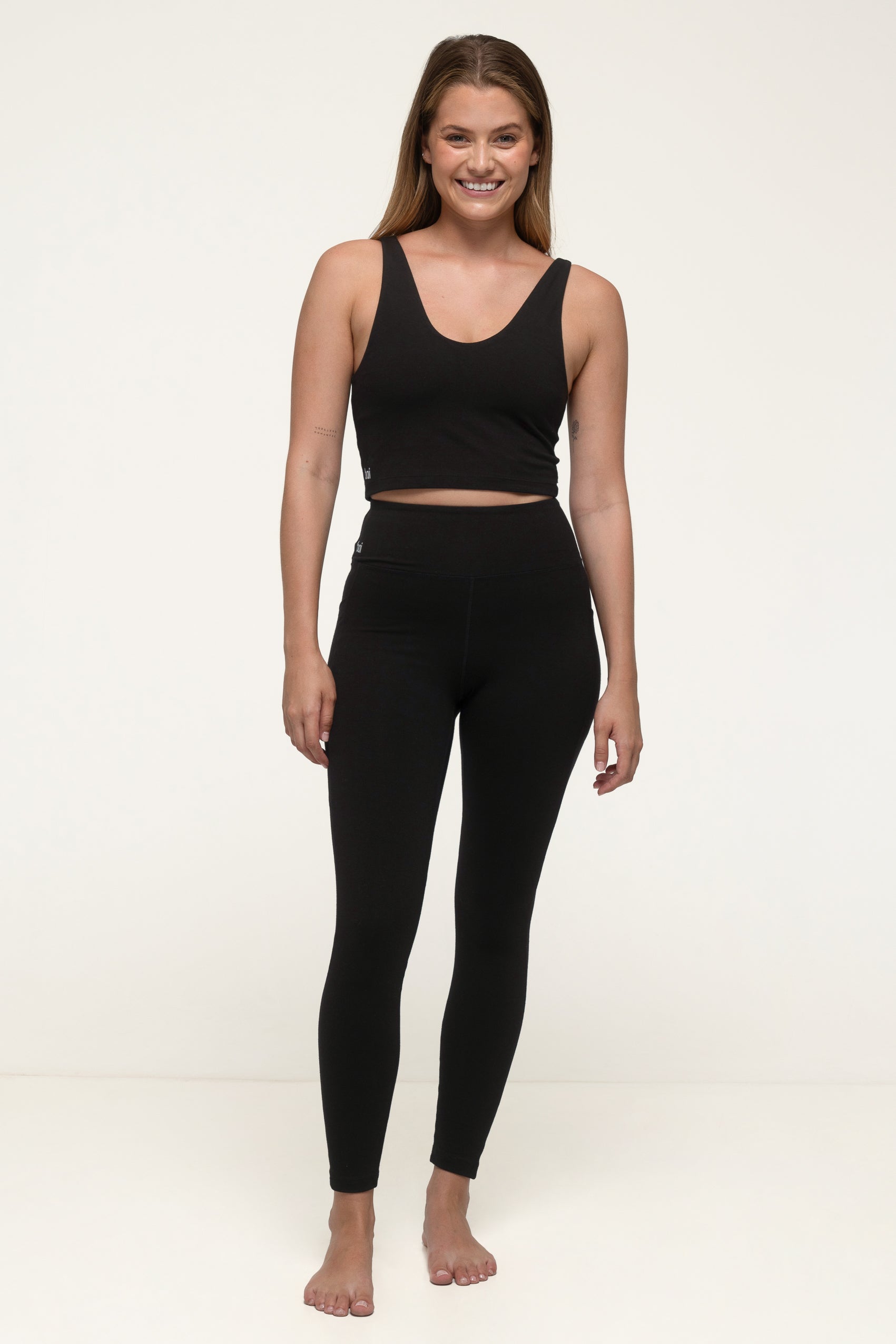 A woman in a black sustainable activewear set wearing thick black leggings with pockets and a eco exercise tank top smiling. #color_black
