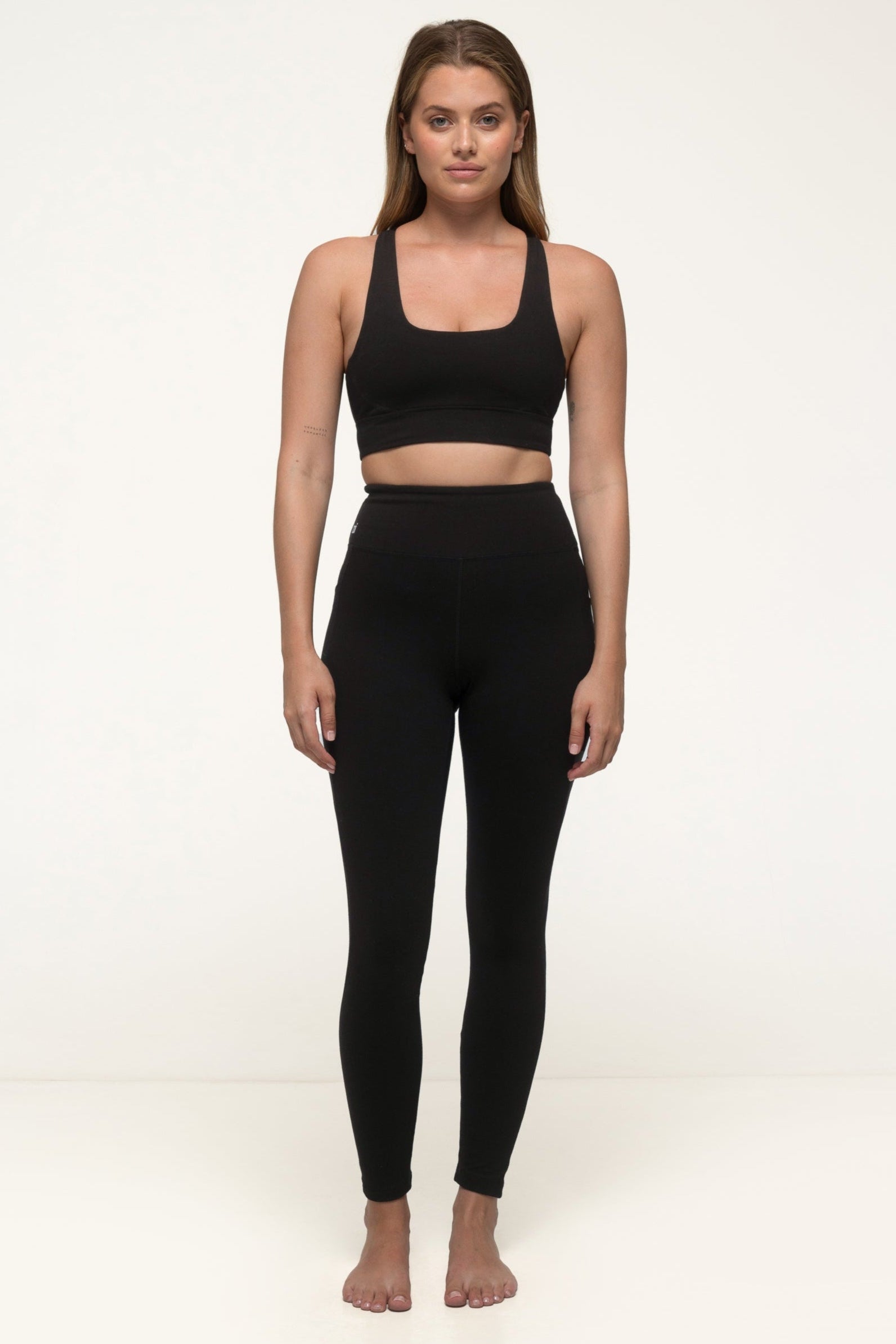 A woman in a black sustainable activewear set wearing thick black leggings with pockets and a eco exercise top. #color_black