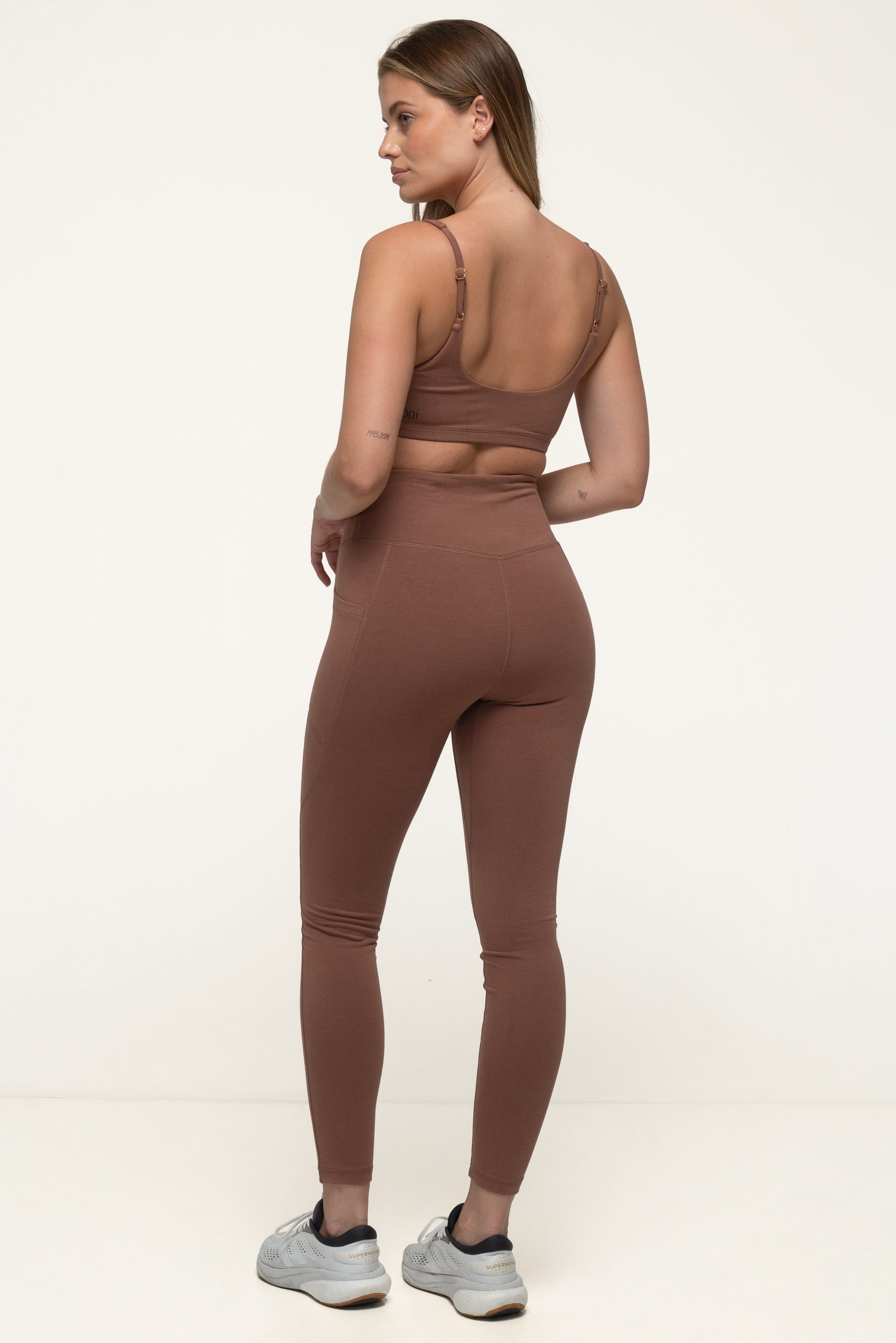 A woman in a cappuccino brown sustainable activewear set wearing high rise soft leggings and an eco yoga top. #color_brown