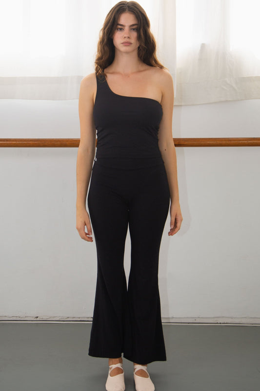 Woman wearing a black one-shoulder top and black flare pants for barre  in a studio setting