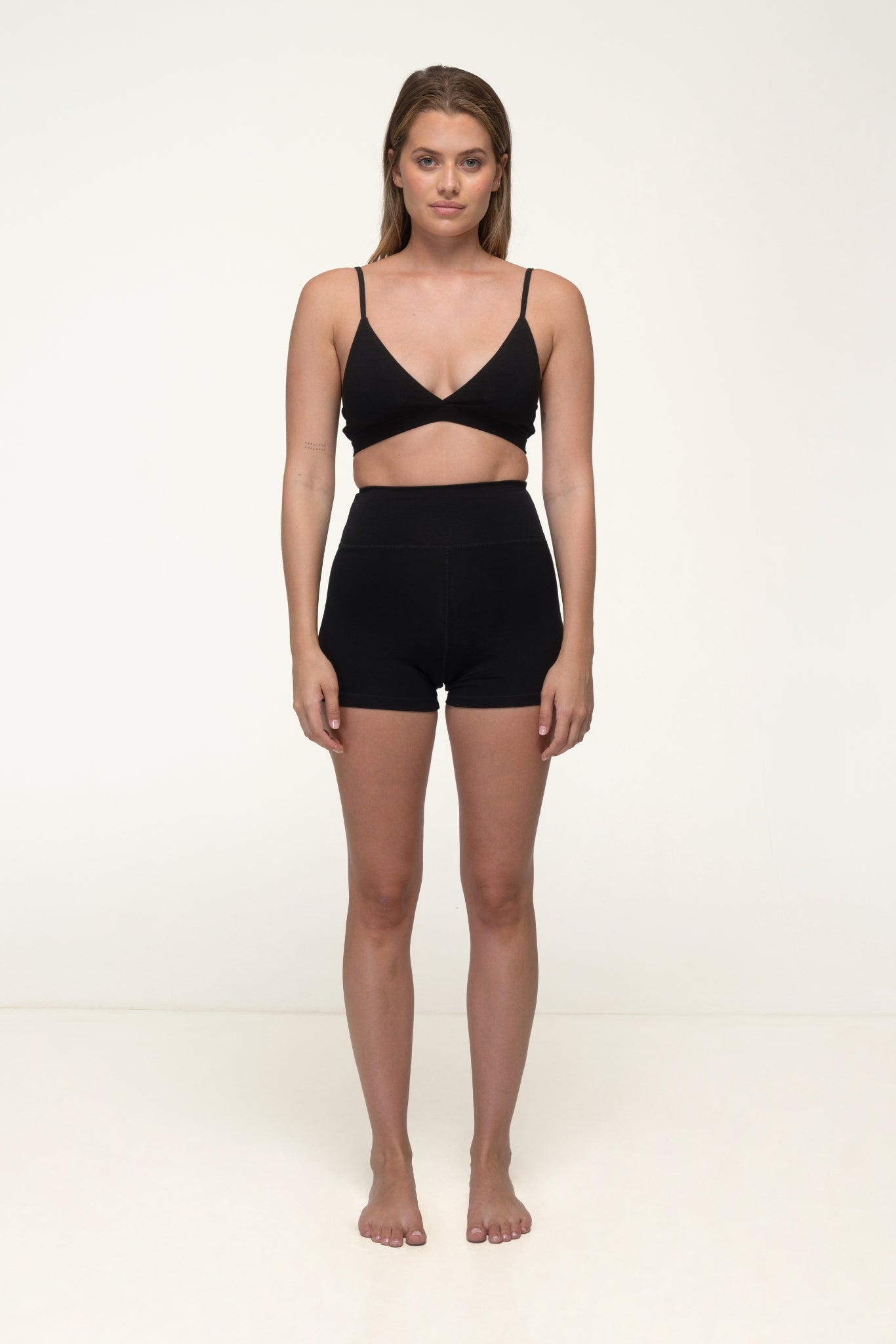 Woman wearing a black bra and high-waisted shorts on a white background