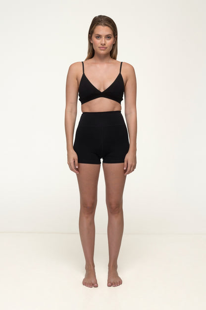 Woman wearing a black bra and high-waisted shorts on a white background