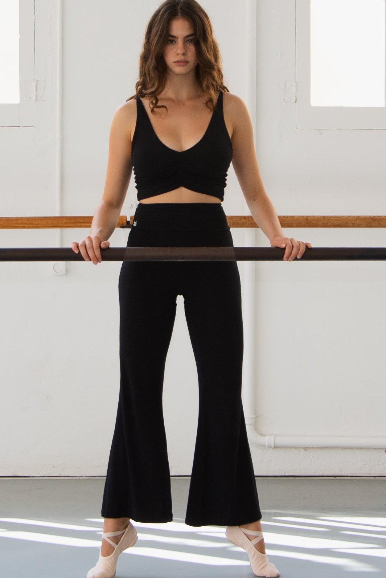 Woman practicing ballet in a studio with large windows in a ruche top in black