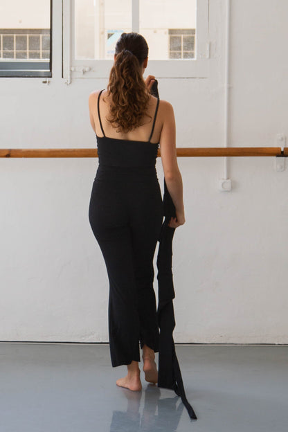 Woman in a black top standing in a dance studio with large windows.