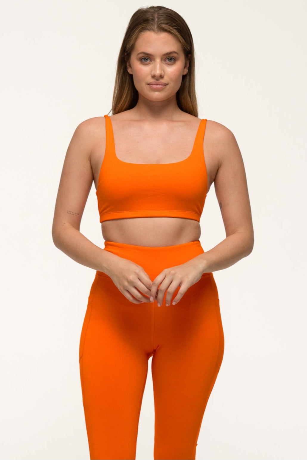 A woman in bai active tangelo orange eco-friendly sports set, wearing high-rise bamboo leggings with pockets and matching eco-friendly crop top. #color_orange