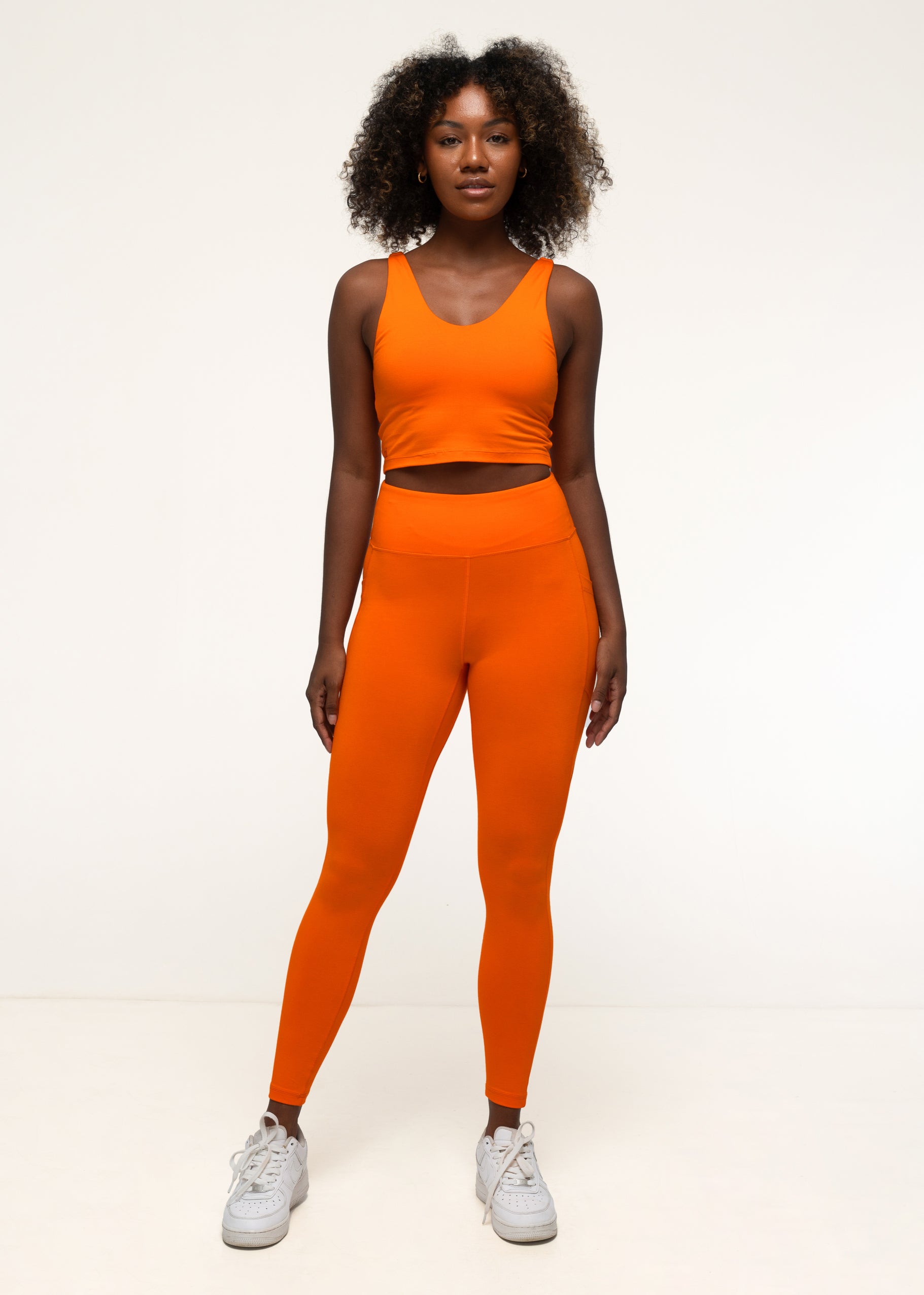A woman wearing bai active bright orange eco-conscious yoga outfit, featuring pocketed high-waist bamboo leggings and a tank top. #color_tangelo-orange
