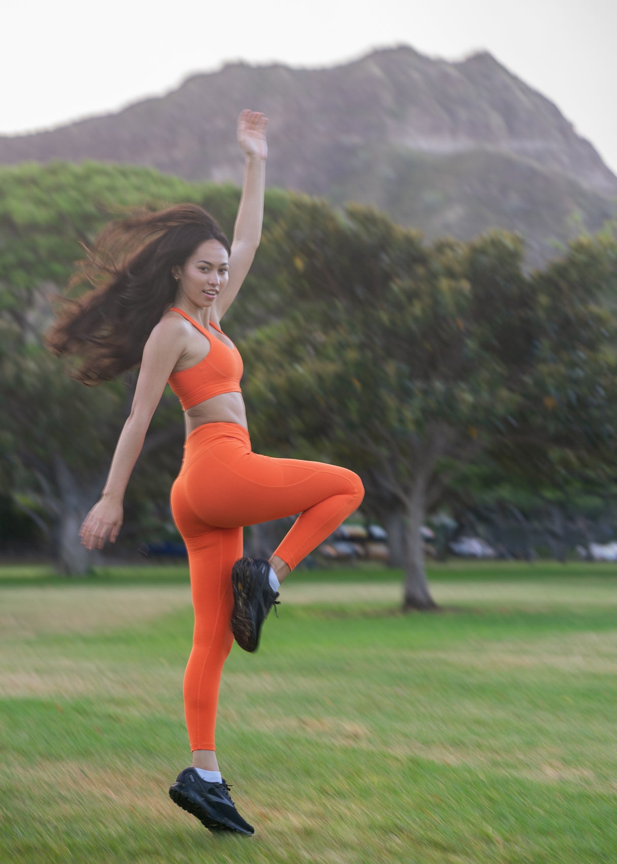Joyful woman jumping in bai active happiness-inducing activewear set made from natural materials, featuring soft bamboo leggings in orange. #color_orange